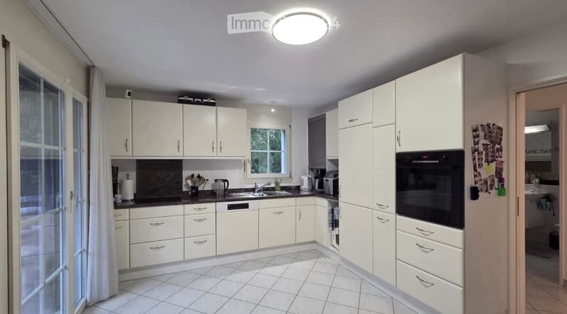 Bright kitchen with white cabinets, black countertops, and tiled flooring. Features a sink, oven, dishwasher, coffee maker, and toaster.