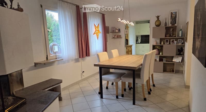 Dining room with a wooden dining table, four chairs, a cabinet with decorative items, and a fireplace.