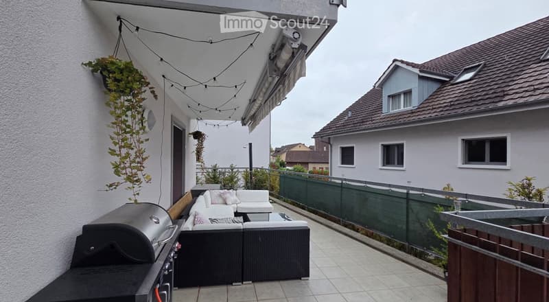 Balcony with a white sofa, small table, and a grill, decorated with hanging plants and string lights.