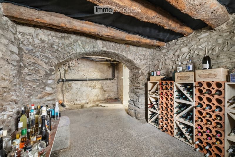 Wine cellar with stone walls, wooden racks filled with wine bottles, and a table holding additional bottles.