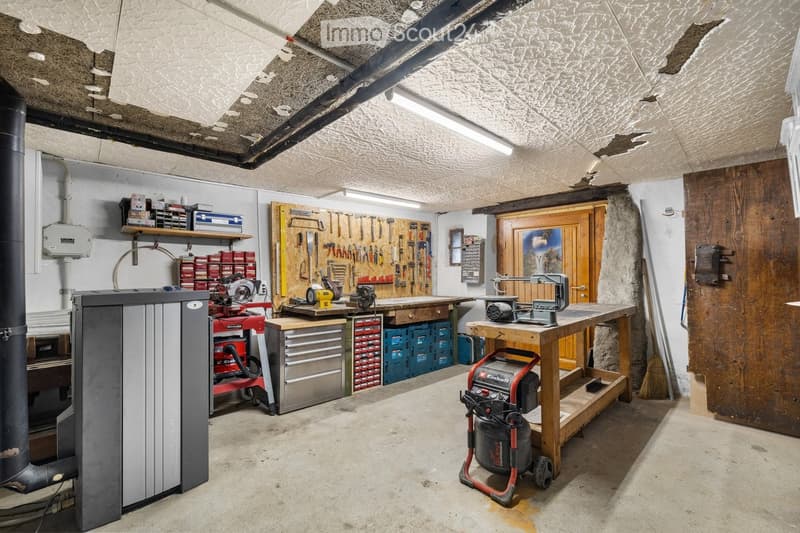 Well-organized workshop with a central workbench, tool wall, storage shelves, and various tools and equipment.