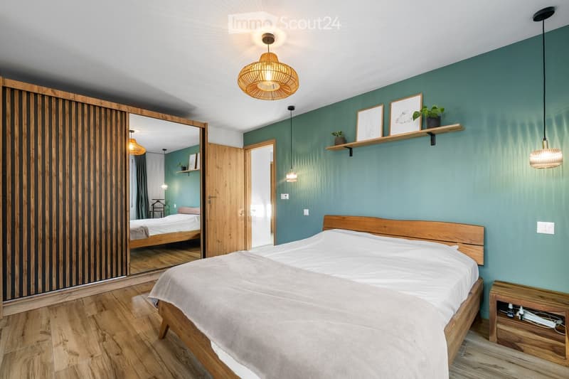 Modern bedroom with a wooden bed, white bedding, a large mirror, pendant lights, and a shelf with decorative items.