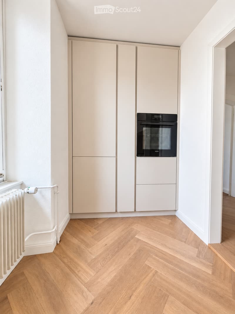 Modern kitchen with light-colored cabinets, a built-in oven, and herringbone wooden flooring.