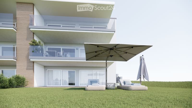 Modern two-story house with balconies, outdoor seating area featuring sun loungers, umbrella, and small table on a grassy lawn.