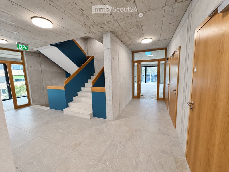 Modern hallway with tiled floor, wooden doors, staircase with blue and white accent, and recessed lighting.