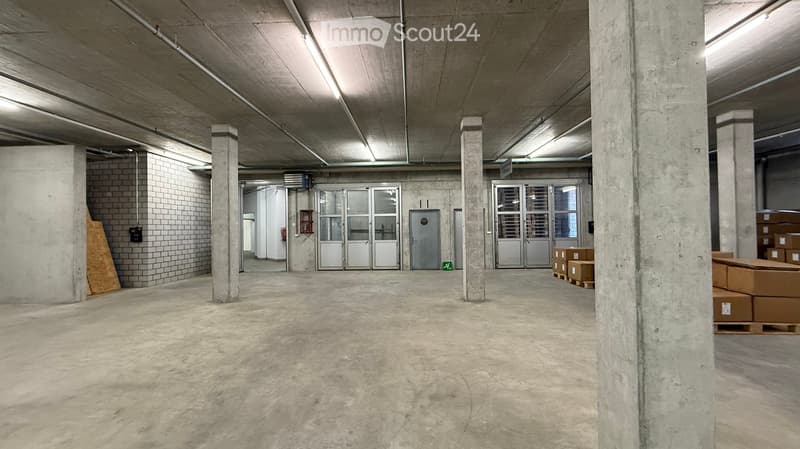 Empty warehouse space with concrete floors, large pillars, and industrial-style doors. No furniture or equipment present.