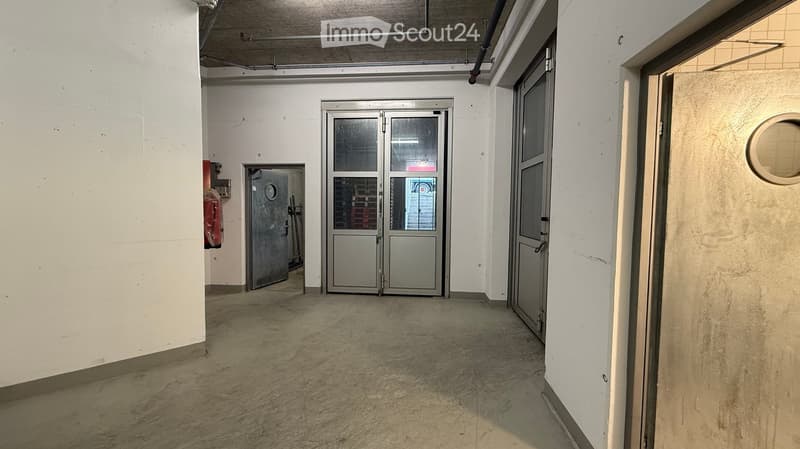 Empty hallway with concrete floor, white walls, and multiple doors including a large industrial-style door with glass panels.