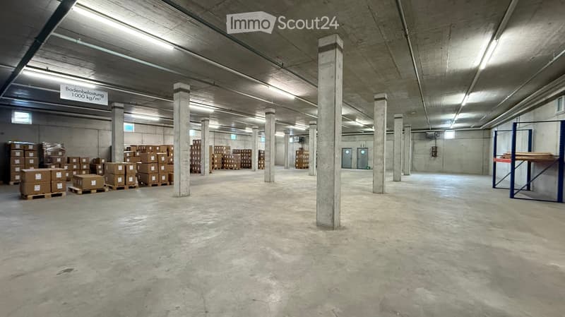 Empty warehouse space with concrete floors and pillars, storage boxes, and a sign indicating floor load capacity.