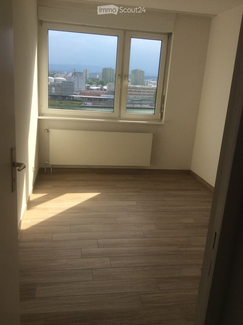 Empty room with wooden flooring, large windows offering a city view, and a radiator below the windows.