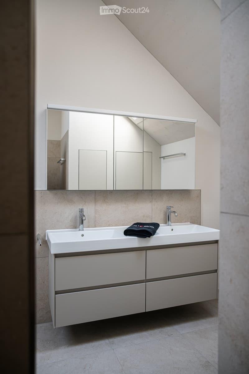 Modern bathroom with a double sink, sleek mirrored cabinet, and a folded black towel on the counter.
