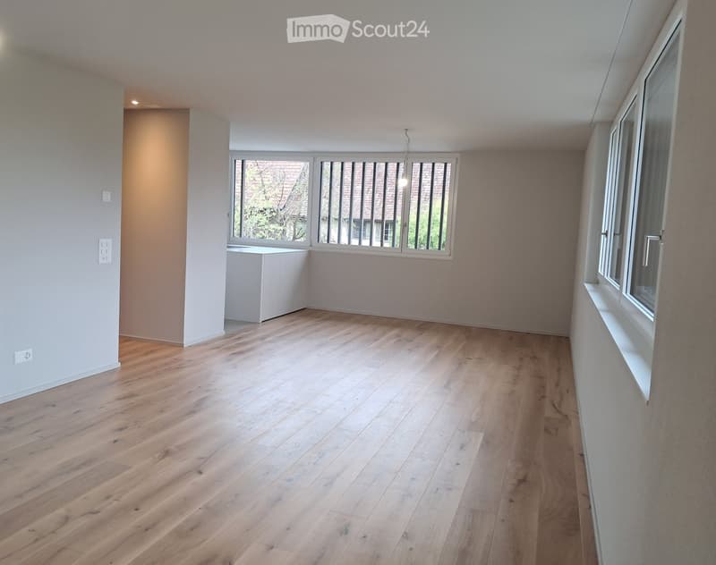 Empty room with light wooden flooring, white walls, and large windows with blinds. No furniture or equipment present.