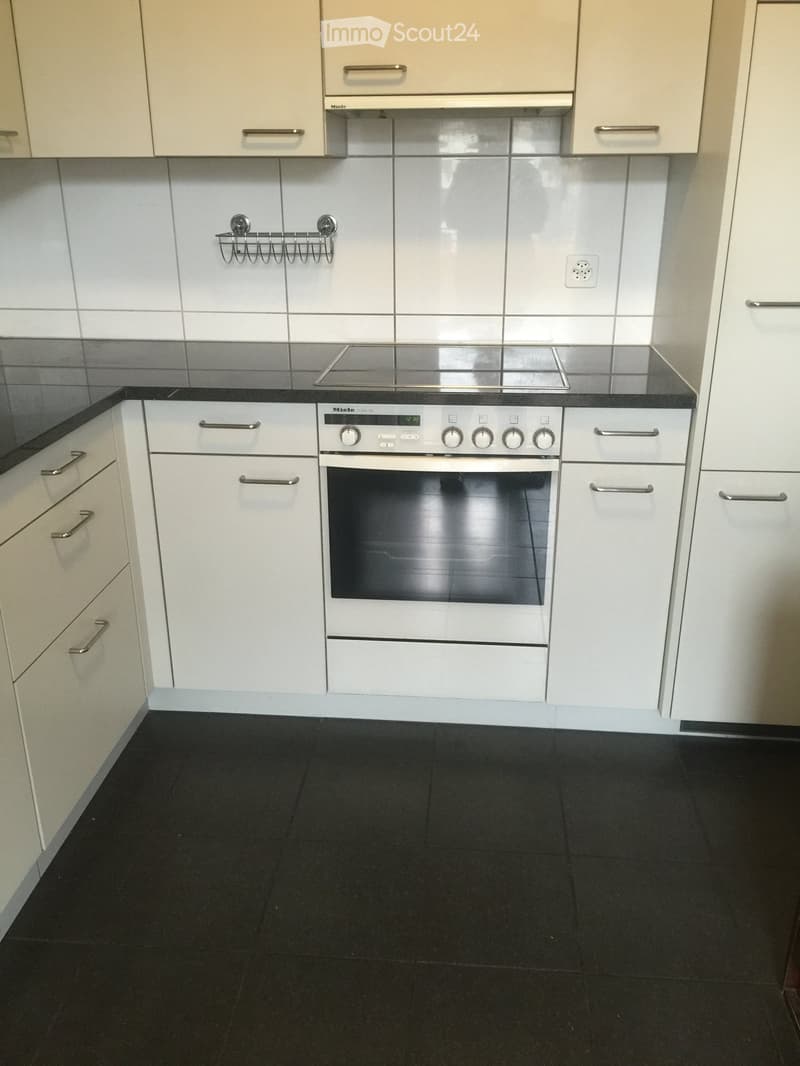Modern kitchen with white cabinets, black countertop, and a built-in oven. The floor is black tiled.