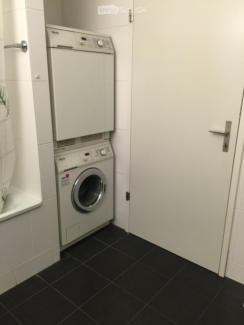 Bathroom with black tiled floor, white walls, and stacked Miele washing machine and dryer unit.