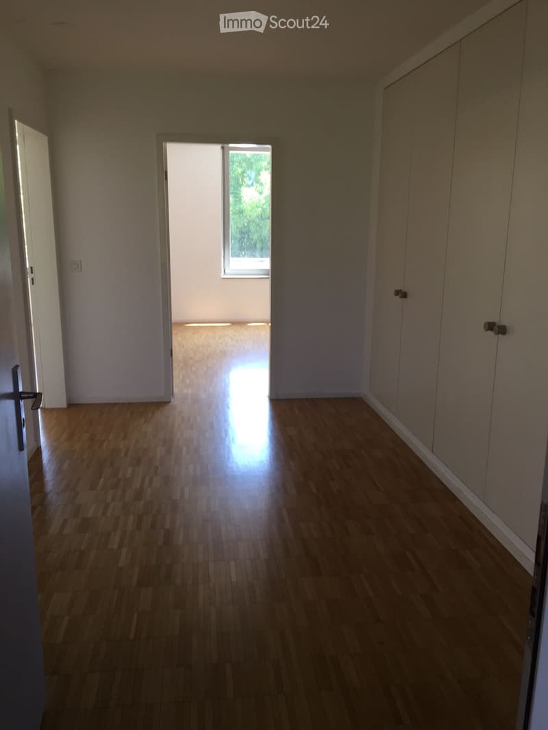 Empty hallway with wooden flooring, white walls, and a window at the end letting in natural light. Doors on both sides lead to other rooms.