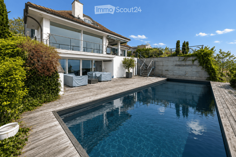 Modern house with a large swimming pool in the garden area, surrounded by wooden decking and lush greenery.