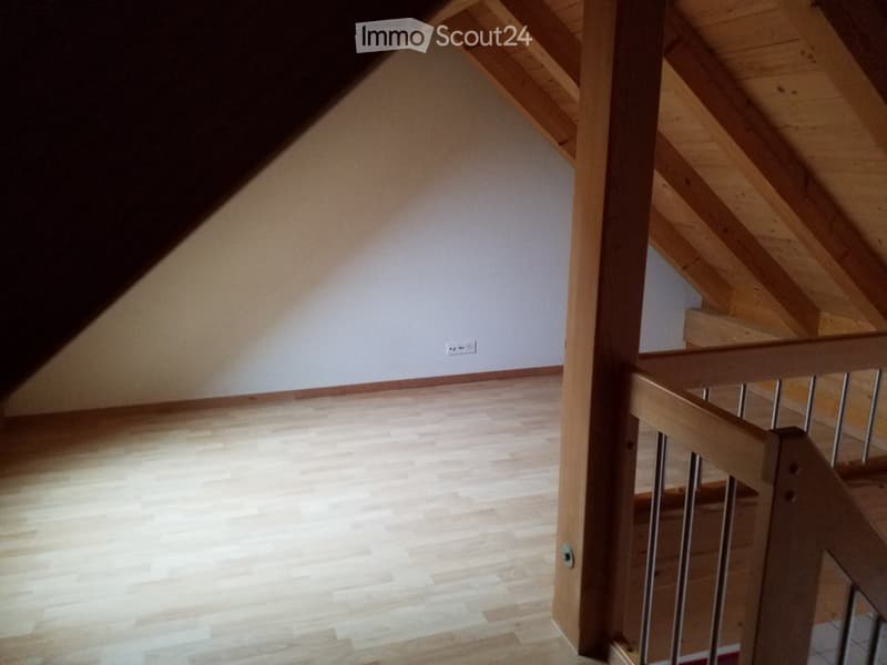 Empty room with wooden flooring and white walls, featuring a staircase with wooden railings and metal balusters.