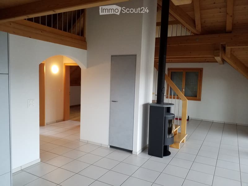 Bright hallway with tiled flooring, white walls, wooden staircase, and a modern wood-burning stove. An arched doorway leads to another room.