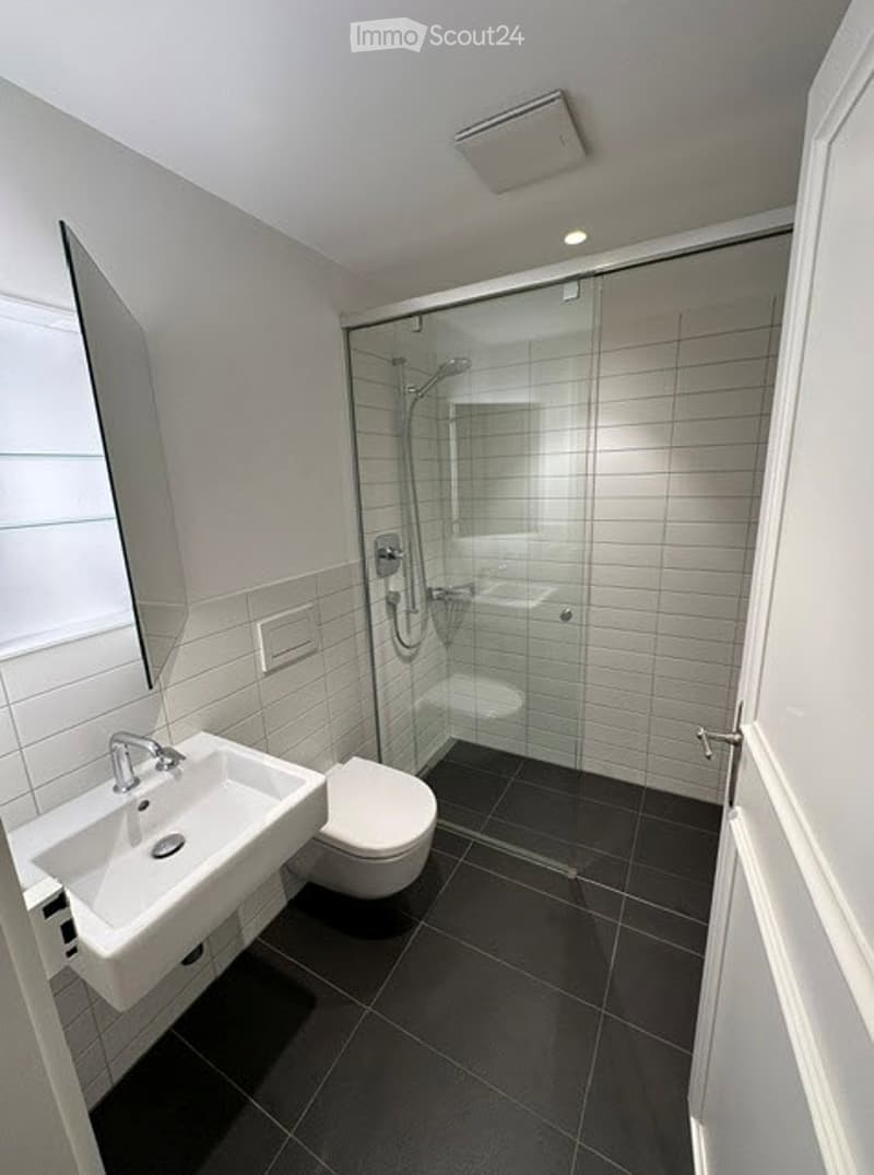 Modern bathroom with white tiles, black floor, glass-enclosed shower, sink, and toilet.