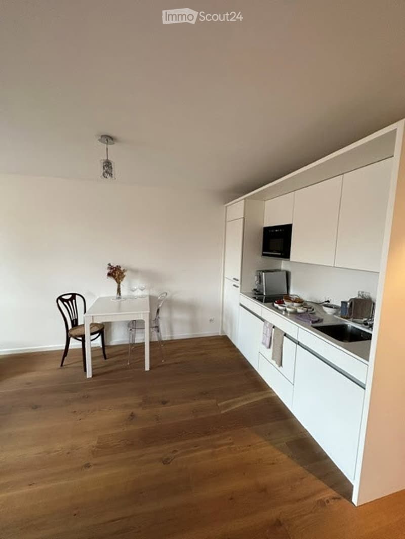 Modern kitchen with white cabinets, stainless steel appliances, and a small dining area with a table and chairs.