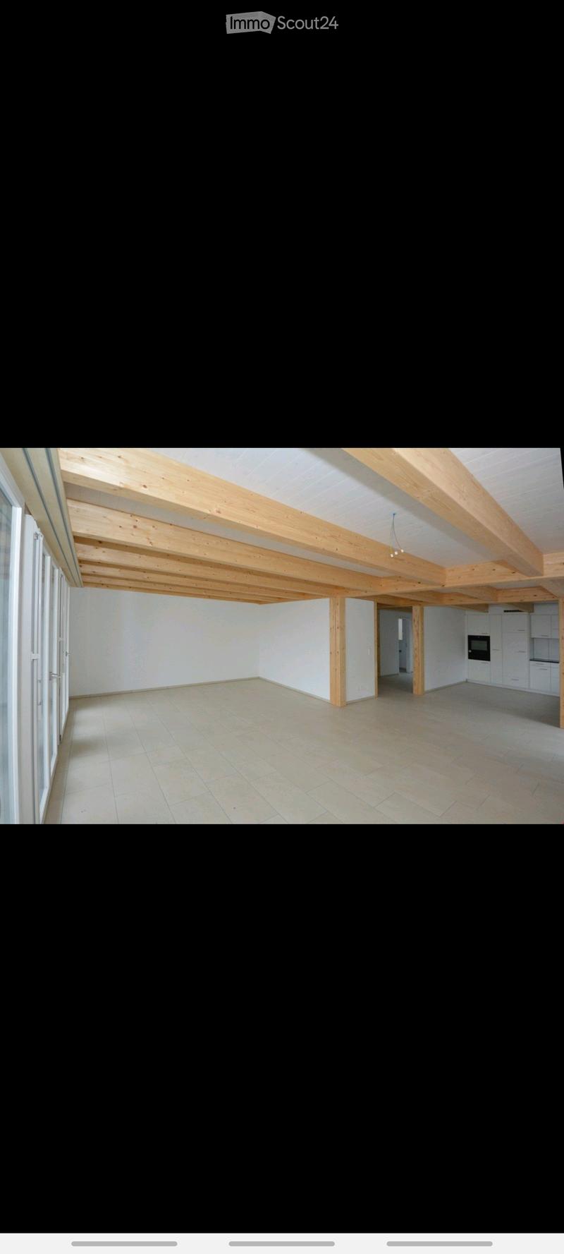 Empty room with wooden beams on the ceiling, tiled floor, and large windows on one side. The space is unfurnished and appears to be a living or dining area.