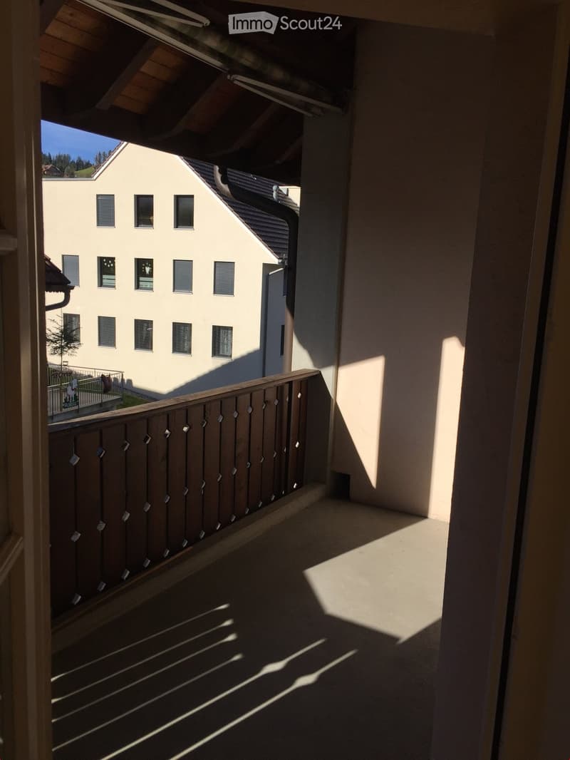 Balcony with wooden railing, overlooking a building with multiple windows and a small garden area.