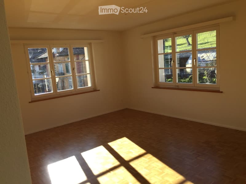 Empty room with wooden flooring and large windows, allowing natural light to fill the space.
