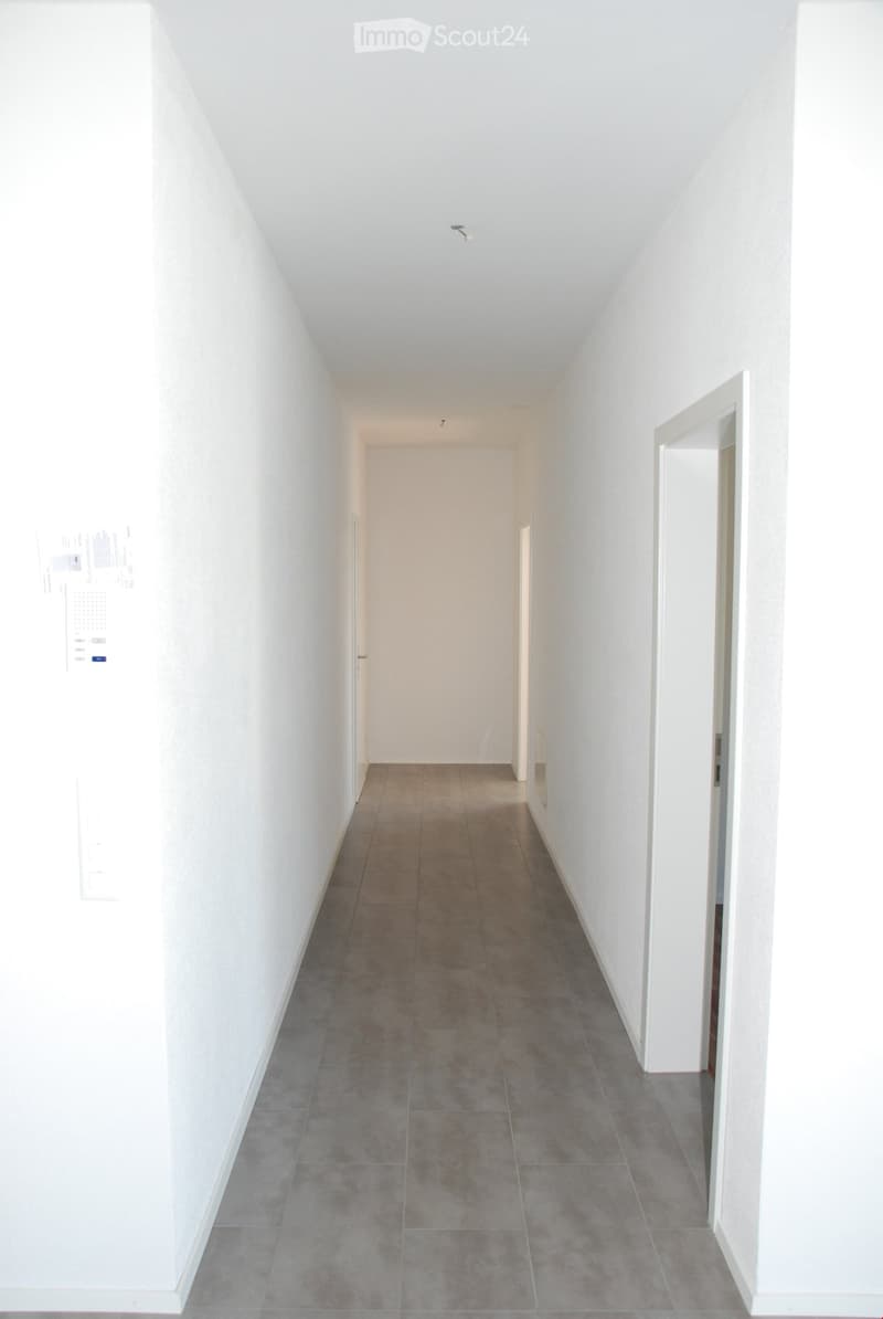 A clean, modern hallway with white walls, gray tiled flooring, and several doors leading to other rooms.