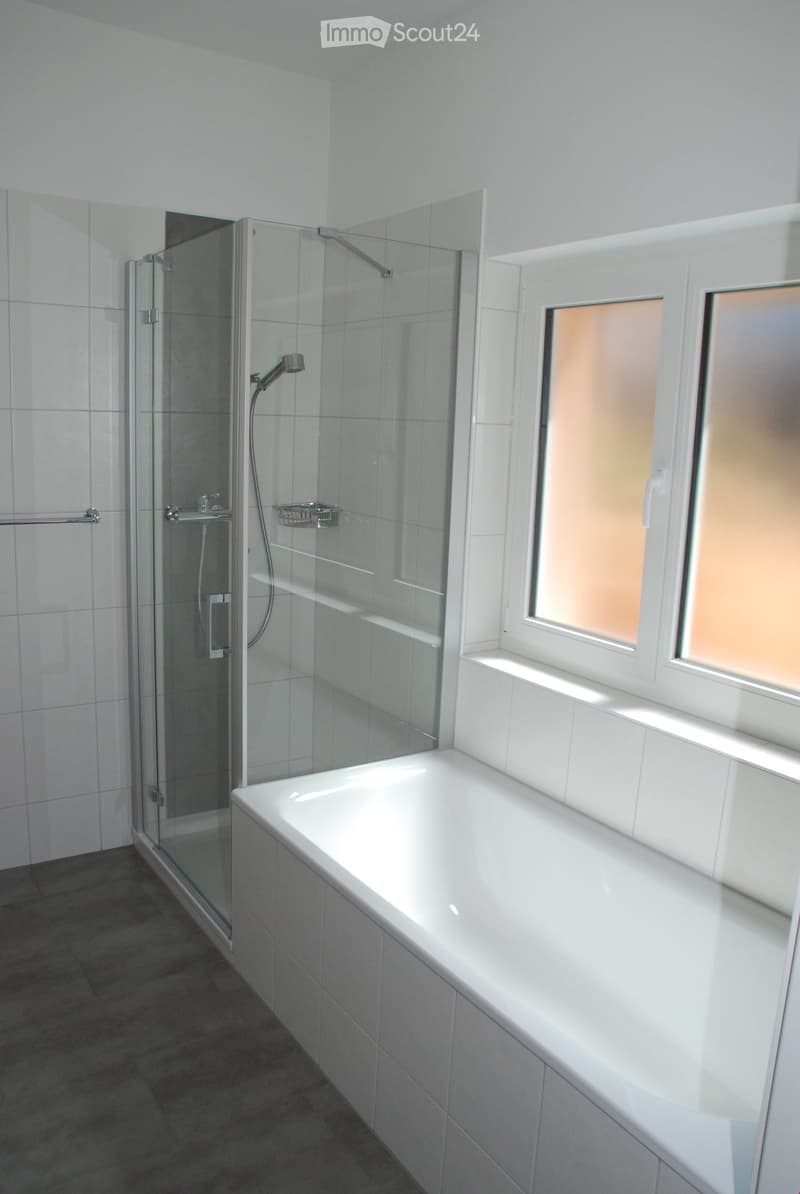 Modern bathroom with a white bathtub, glass-enclosed shower, and tiled walls and floor.