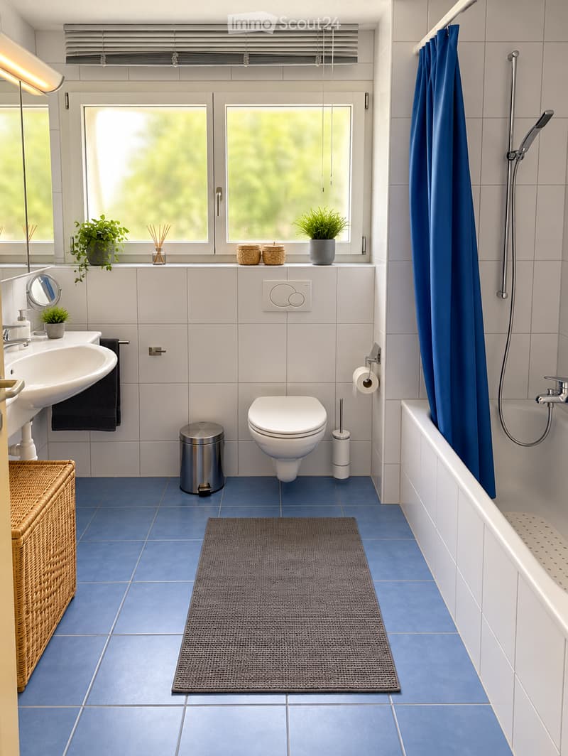 Modern bathroom with blue tiles, white fixtures, a bathtub with a shower curtain, a sink, a toilet, a trash can, a bath mat, and decorative plants and candles on the windowsill.