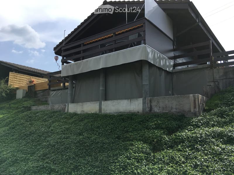 Two-story house with a raised ground floor, balcony, and covered outdoor area. The structure features a modern design with a concrete base and wooden elements.
