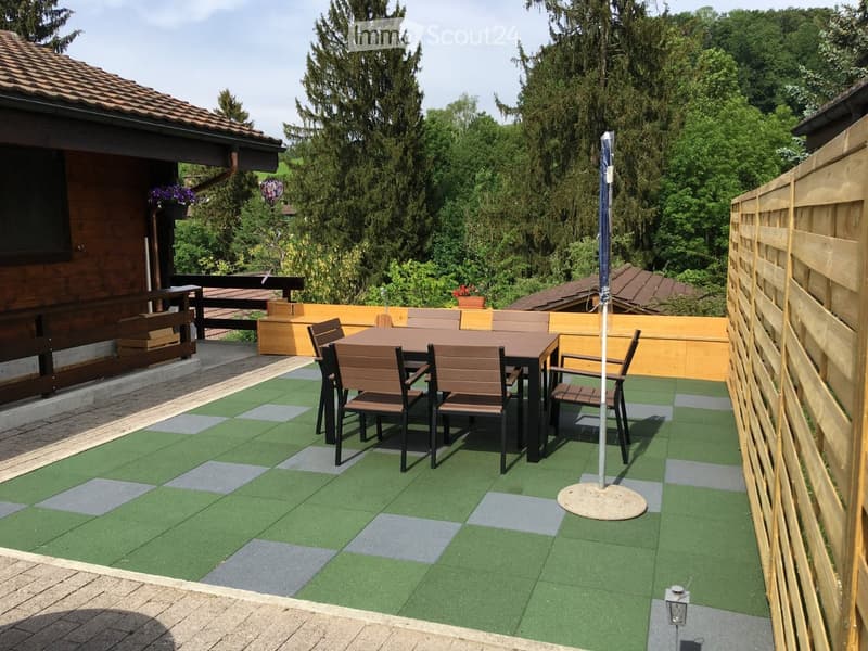 Outdoor patio with artificial grass flooring, a wooden table and chairs, an umbrella pole, and a wooden fence.