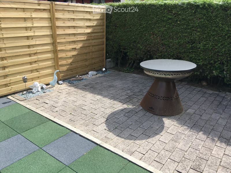 Garden area with a round table, decorative statues, a wooden fence, and a neatly trimmed hedge.