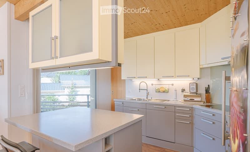 Modern kitchen with light-colored cabinets, a central island, and stainless steel appliances. Features include a sink with a modern faucet, a refrigerator, and a toaster on the counter.