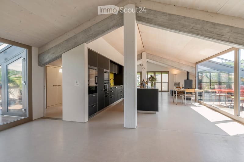 Open-plan living and dining area with modern kitchen, dining table, and chairs, large windows, and exposed wooden beams.