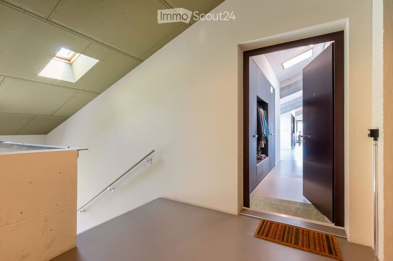 Modern hallway with white walls, a skylight, a staircase with a metal railing, and an open door leading to another room.