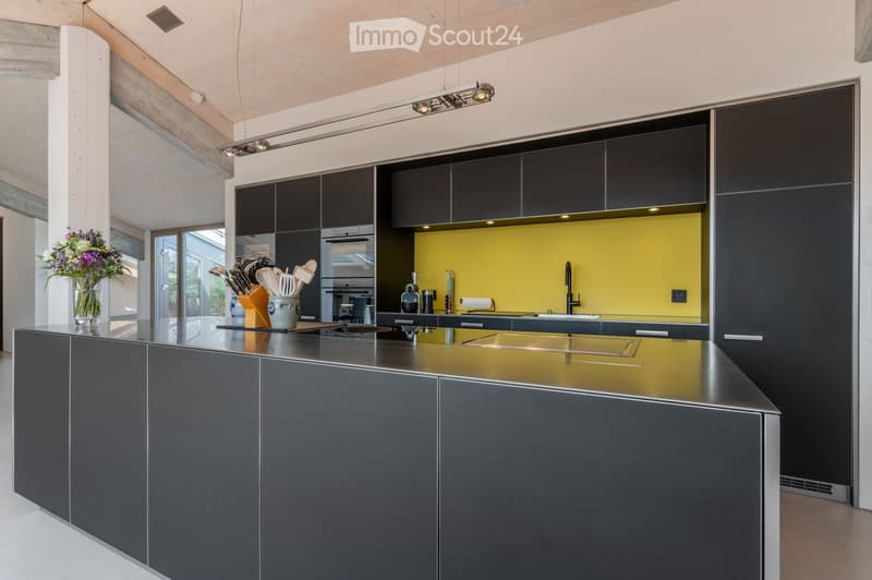 Modern kitchen with dark grey cabinets, stainless steel island, yellow accent wall, and various appliances.