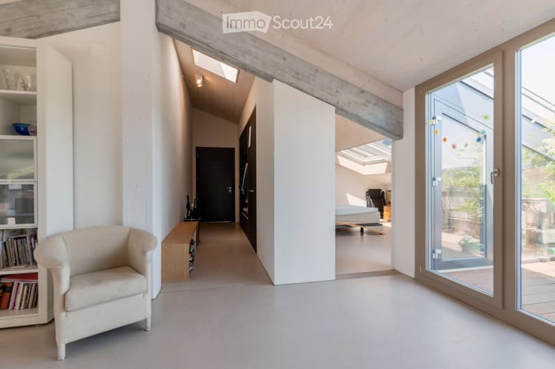 Modern hallway with white walls, concrete ceiling beams, large glass doors leading to a bedroom area, and a small seating area with a chair and shelf.