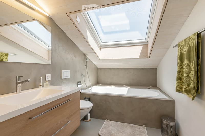 Modern bathroom with skylight windows, wooden vanity with sink and faucet, bathtub, toilet, and decorative towels.
