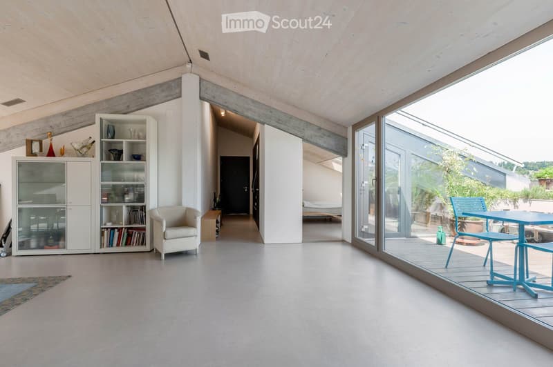 Modern living space with a large open area, white cabinetry, a comfortable armchair, and a view to a balcony or terrace area with outdoor furniture.