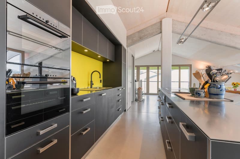Modern kitchen with grey cabinets, stainless steel appliances, and a bright yellow accent wall. Features an oven, countertop, and various kitchen utensils.