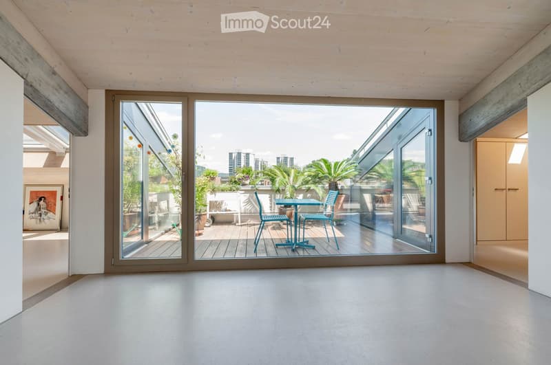 Bright, minimalist room with large glass doors opening to a balcony, featuring a small table and chairs, modern decor, and a view of greenery and cityscape.