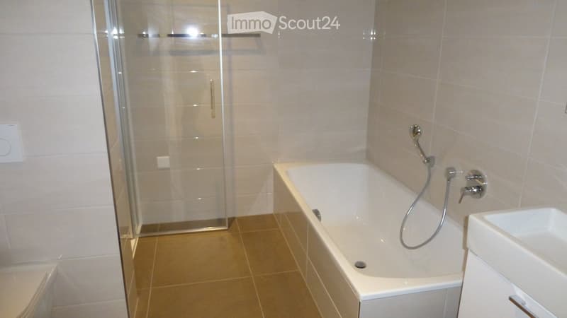 Modern bathroom with a bathtub, shower, sink, and toilet. Features light-colored tiles and a glass-enclosed shower area.
