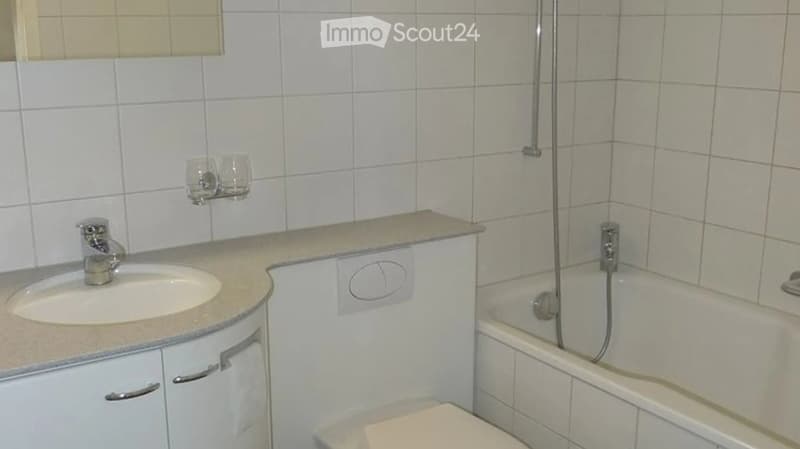 Bathroom with a sink, faucet, bathtub, toilet, and cabinet. The walls are tiled, and there is a showerhead above the bathtub.