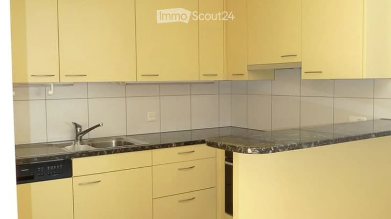 Modern kitchen with light yellow cabinets, granite countertop, stainless steel sink, and built-in dishwasher.