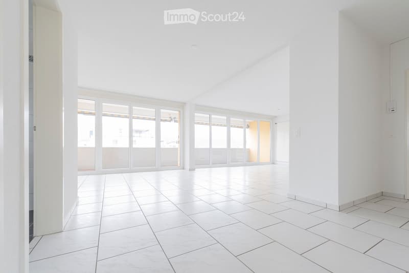 Empty room with white tiled flooring and white walls, featuring large glass sliding doors leading to a balcony area.