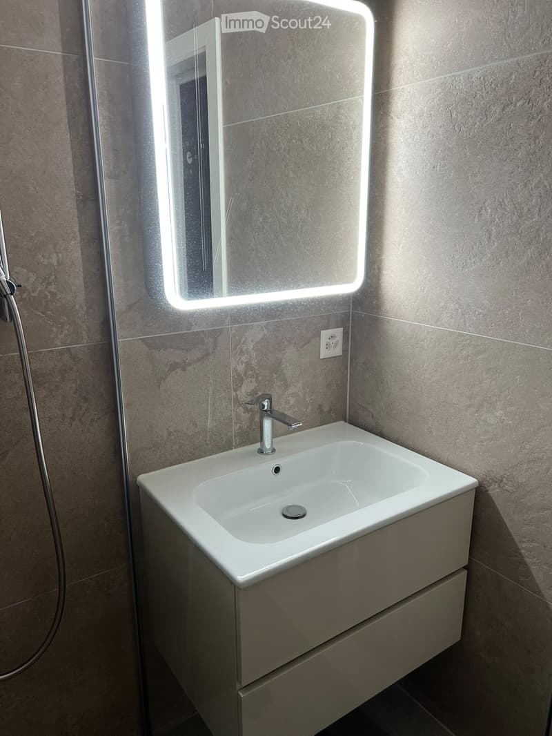 Modern bathroom with a white sink, chrome faucet, illuminated mirror, and a built-in cabinet below the sink.