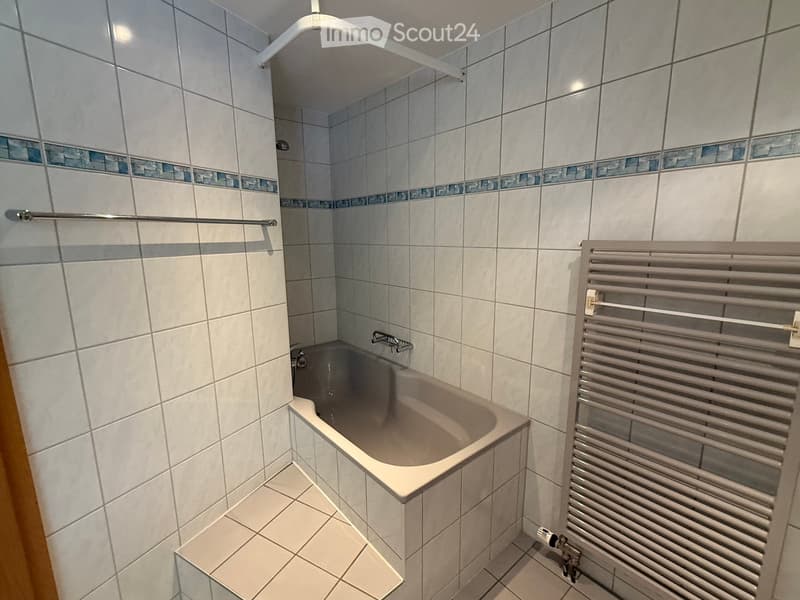 Modern bathroom with a bathtub, tiled walls, a radiator, and a shower rail.