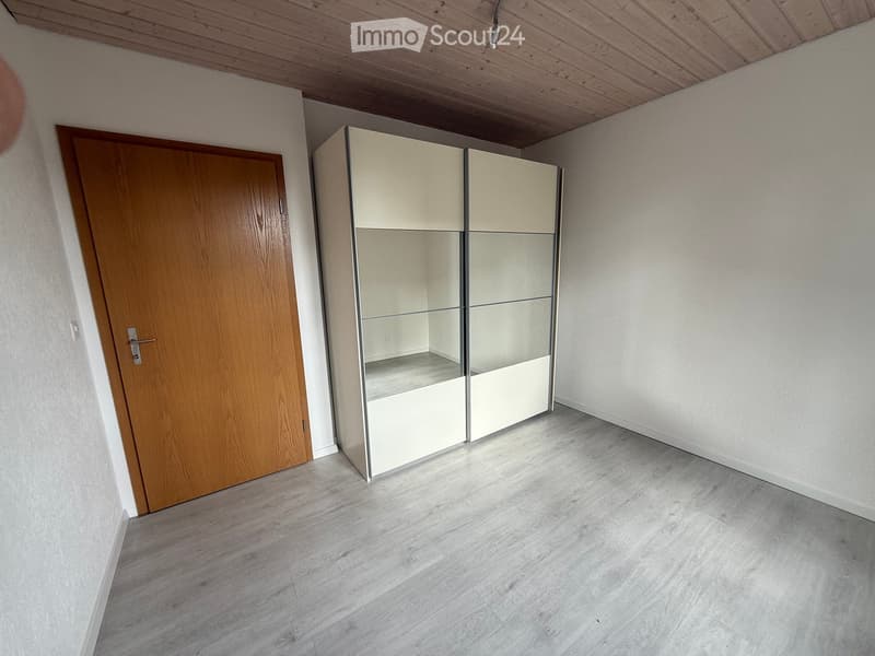 Empty room with light-colored wooden floor, white walls, a wooden door, and a built-in closet with mirrored doors.