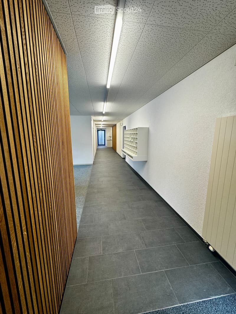 Modern hallway with grey tiled flooring, white walls, and a wooden panel accent wall. Features a built-in white shelving unit and a recessed ceiling light.