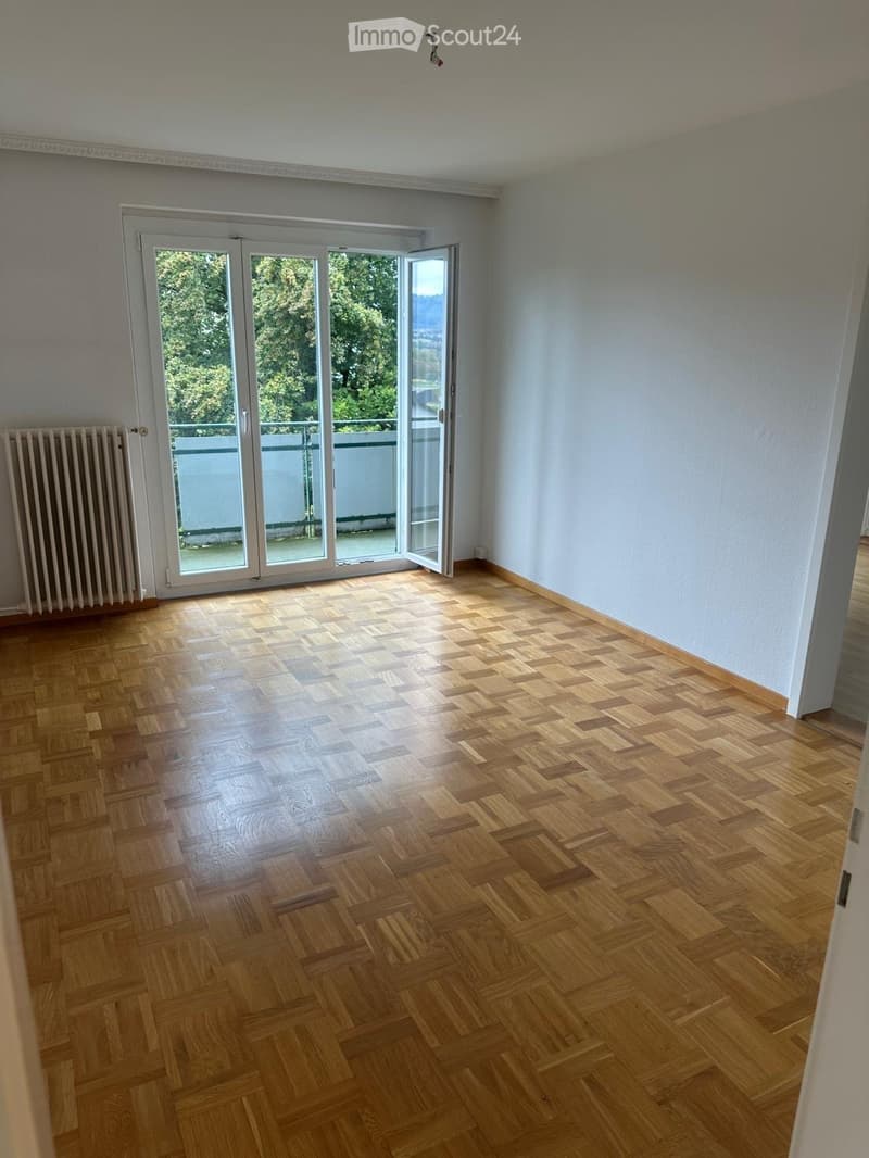 Empty room with wooden parquet flooring, white walls, and large glass sliding doors leading to a balcony.